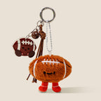 A plush American football keychain with a smiling face and red feet, attached to a keyring with a matching acrylic football charm and a brown bell.