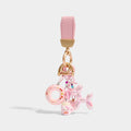 A keychain with a pink leather strap and gold-tone hardware, holding a set of charms including a pink inflatable ring with floral patterns, a pink Hello Kitty-themed mug, and a shiny pink iridescent balloon dog.