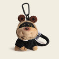 A plush dog bag charm with brown crocheted bear ears on its hood, attached to a black carabiner clip. The charm has a smiling face and is dressed in a black outfit, making it a charming and whimsical addition to any bag or keychain.