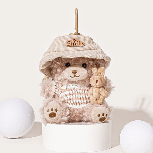 A light brown teddy bear plush keychain wearing a beige corduroy bucket hat with a "Smile" patch and a beige and white striped knit sweater, holding a small beige rabbit plush, attached to a beige carabiner clip.