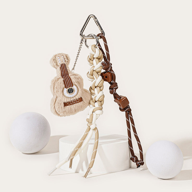 A beige plush guitar keychain with brown string embroidery, attached to a silver carabiner with a mixed brown and white braided rope strap and brown star-shaped beads.
