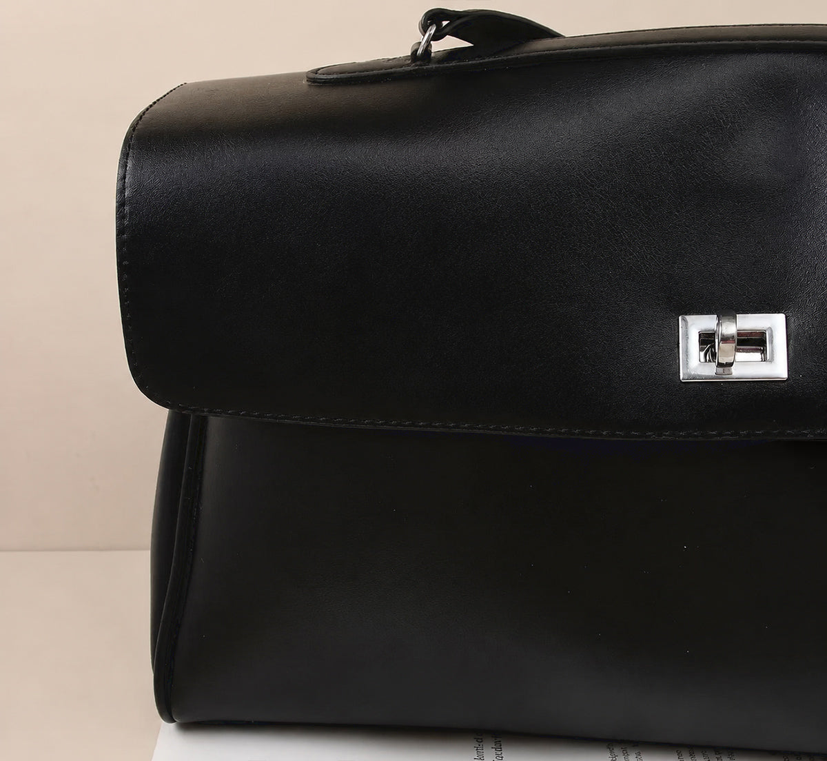 A minimalist black leather handbag with a sleek silver-tone clasp, shown without any accessories or charms, emphasizing its clean lines and structured silhouette against a neutral background.