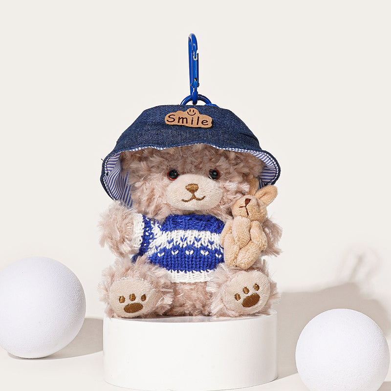 A fluffy light brown teddy bear plush keychain wearing a blue denim bucket hat with a "Smile" patch and a blue and white knit vest, holding a small beige rabbit plush, attached to a blue carabiner clip.