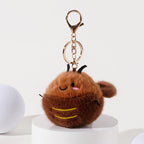 A brown plush cockroach keychain with embroidered facial features, black antennae, and a fuzzy texture, attached to a gold-tone metal carabiner and keyring.
