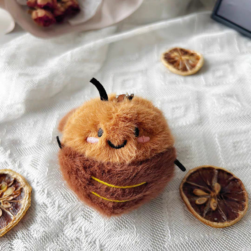 A brown plush cockroach toy with embroidered smiling face, pink cheeks, and black antennae, placed on a white textured fabric with dried orange slices nearby.
