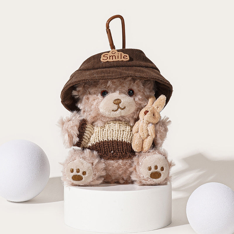 A light brown teddy bear plush keychain wearing a brown corduroy bucket hat with a "Smile" patch and a brown and beige striped knit sweater, holding a small beige rabbit plush, attached to a brown carabiner clip.