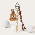 A brown plush guitar-shaped keychain with embroidered strings and soundhole, attached to a silver carabiner with a white and beige braided rope strap and brown decorative beads.