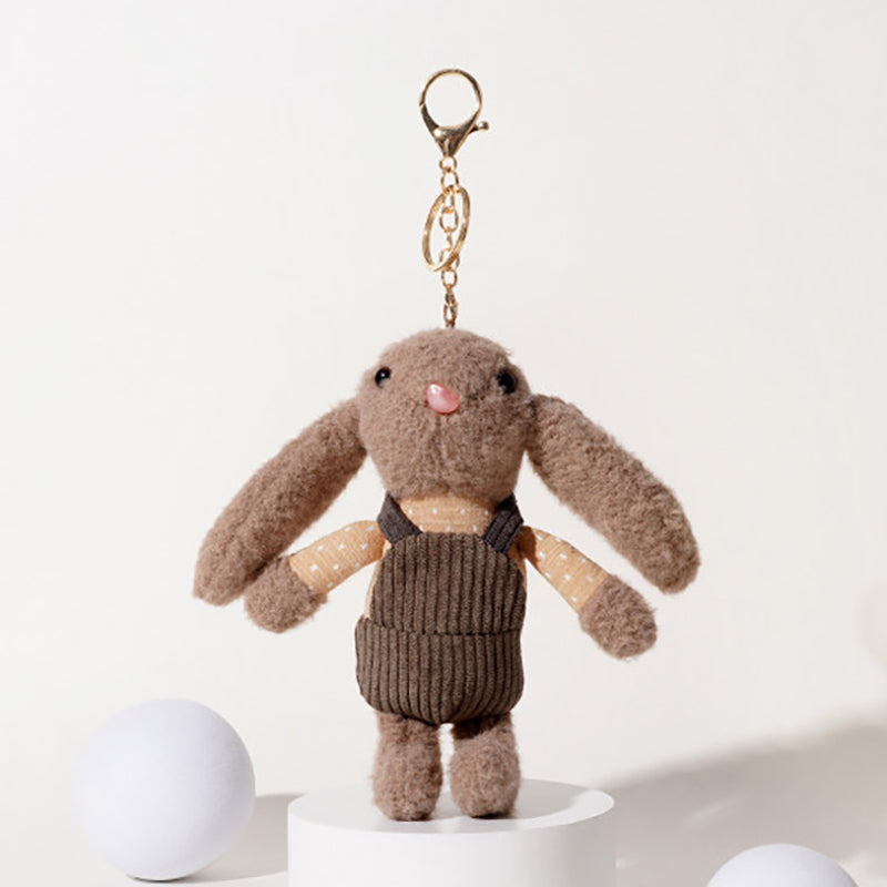 A brown plush rabbit keychain with long floppy ears, black embroidered eyes, and a pink nose, wearing a beige polka-dot shirt and a brown corduroy vest, attached to a gold-tone metal carabiner and keyring, displayed on a white pedestal.