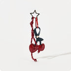 A burgundy leather cherry-shaped bag charm with a dark blue stem, attached to a matching burgundy braided rope strap. A black star-shaped clip is at the top, designed as a stylish and adorable accessory for bags or keychains.