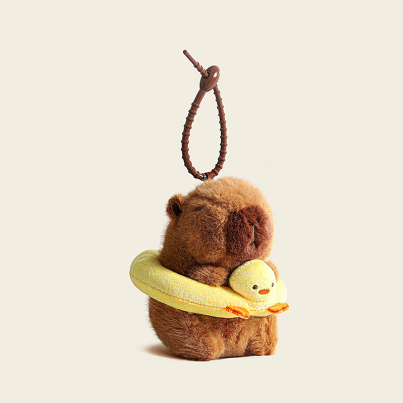A plush capybara bag charm holding a yellow swim ring with a small duck design, attached to a brown carabiner clip. This adorable accessory is perfect for adding a playful touch to bags or keychains.