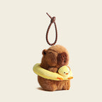 A plush capybara bag charm holding a yellow swim ring with a small duck design, attached to a brown carabiner clip. This adorable accessory is perfect for adding a playful touch to bags or keychains.