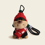 A plush dog bag charm wearing a red knitted hat with green pompoms and a matching red scarf with white patterns, attached to a black carabiner clip. This festive and cozy accessory is ideal for adding a touch of holiday cheer to bags or car interiors.