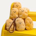 A group of cute plush potato keychains with simple smiling faces, arranged on a yellow chair. One keychain in the foreground features a brown leather strap with a woven detail and a small leather tag with a smiley face logo, showcasing the design of these trendy and adorable accessories.