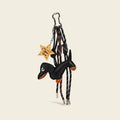 A black leather dachshund bag charm with orange accents on its paws and snout, attached to a silver cloud-shaped carabiner. It features two woven ropes—one white with black stripes, one black with white stripes—tied in knots, and a wooden star-shaped tag engraved with "You're a Star".