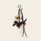 A brown leather dachshund bag charm with orange accents on its paws and snout, attached to a silver cloud-shaped carabiner. It features two woven ropes—one white with black stripes, one brown with white stripes—tied in knots, and a wooden star-shaped tag engraved with "You're a Star".