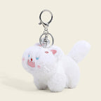 A fluffy white cat plush bag charm with light blue eyes, a pink tongue sticking out, and a small red mark on its forehead. It is attached to a silver lobster clasp and keyring, designed as a cute and trendy accessory for bags or keychains.