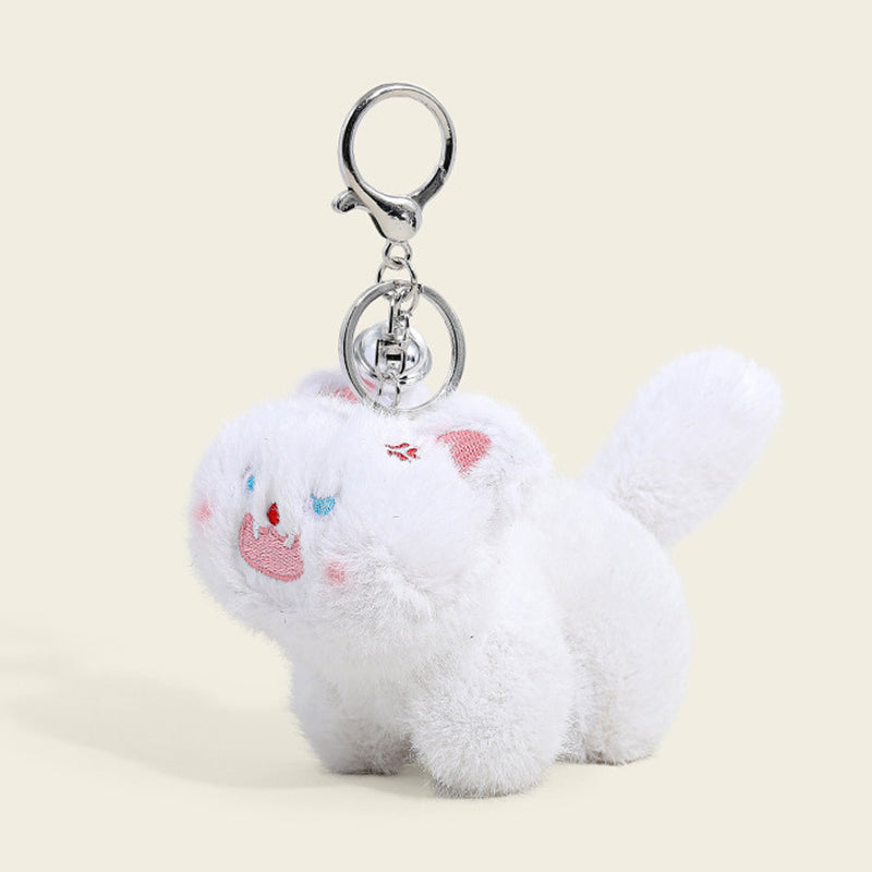 A fluffy white cat plush bag charm with light blue eyes, a pink tongue sticking out, and a small red mark on its forehead. It is attached to a silver lobster clasp and keyring, designed as a cute and trendy accessory for bags or keychains.