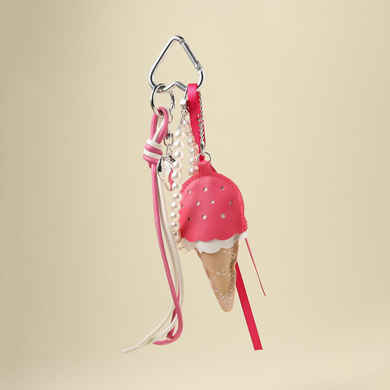 A fuchsia leather ice cream cone bag charm with a white scalloped edge and perforated details, attached to a silver carabiner clip. It features fuchsia and white ribbons, a pearl chain, and a small silver heart charm, designed as a cute and trendy accessory for bags or keychains.