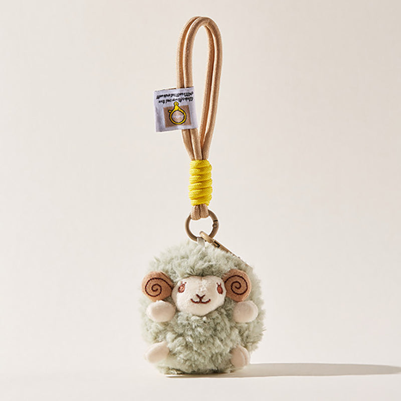 A front-facing view of a light green fluffy sheep plush keychain with brown spiral horns and a smiling face, attached to a beige cord with a yellow wrap and a small branded tag.