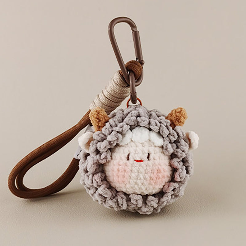 A front view of a grey crocheted sheep keychain with brown horns and a smiling face, hanging from a brown strap.
