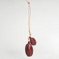 A hanging view of a handcrafted leather charm shaped like two coffee beans. The beans are dark brown with lighter stitching details and are suspended from a natural tan leather cord against a white background.