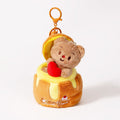 A plush teddy bear bag charm in brown, holding a red heart, nestled inside a honey jar-shaped container with a yellow rim and dripping honey details. The jar has a zipper closure and is attached to an orange lobster clasp and keyring, designed as a cute and sweet accessory for bags or keychains.
