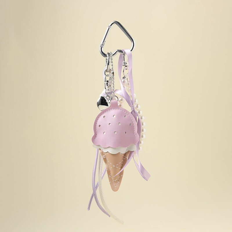 A lavender leather ice cream cone bag charm with a white scalloped edge and perforated details, attached to a silver carabiner clip. It features lavender and white ribbons, a pearl chain, and a small silver heart charm, designed as a cute and trendy accessory for bags or keychains.