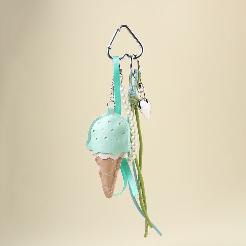 A mint green leather ice cream cone bag charm with a white scalloped edge and perforated details, attached to a silver carabiner clip. It features mint green and light green ribbons, a pearl chain, and a small silver heart charm, designed as a cute and trendy accessory for bags or keychains.