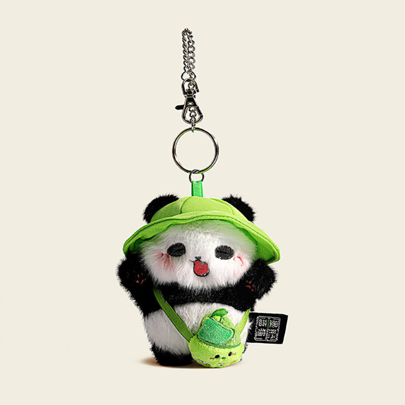 A plush panda bag charm wearing a green bucket hat and carrying a small green bag shaped like a bamboo shoot. The panda has black eyes, a red tongue, and pink cheeks, attached to a silver lobster clasp and keyring, designed as a cute and trendy accessory for bags or keychains.