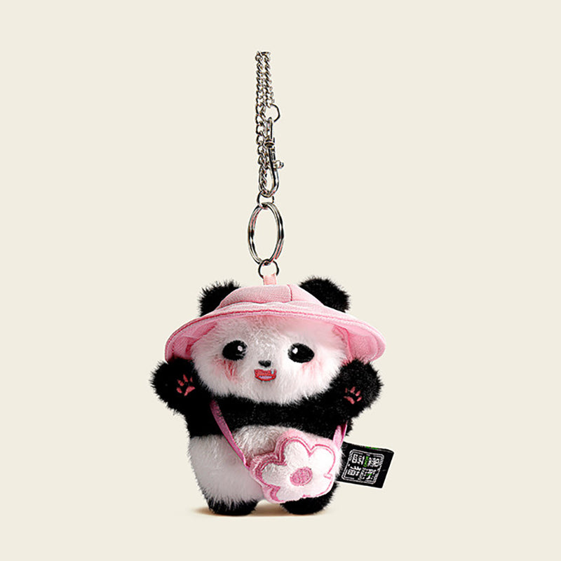 A plush panda bag charm wearing a pink bucket hat and carrying a small pink bag shaped like a flower. The panda has black eyes, a red tongue, and pink cheeks, attached to a silver lobster clasp and keyring, designed as a cute and trendy accessory for bags or keychains.