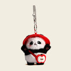 A plush panda bag charm wearing a red bucket hat and carrying a small red bag shaped like an apple. The panda has black eyes, a red tongue, and pink cheeks, attached to a silver lobster clasp and keyring, designed as a cute and trendy accessory for bags or keychains.