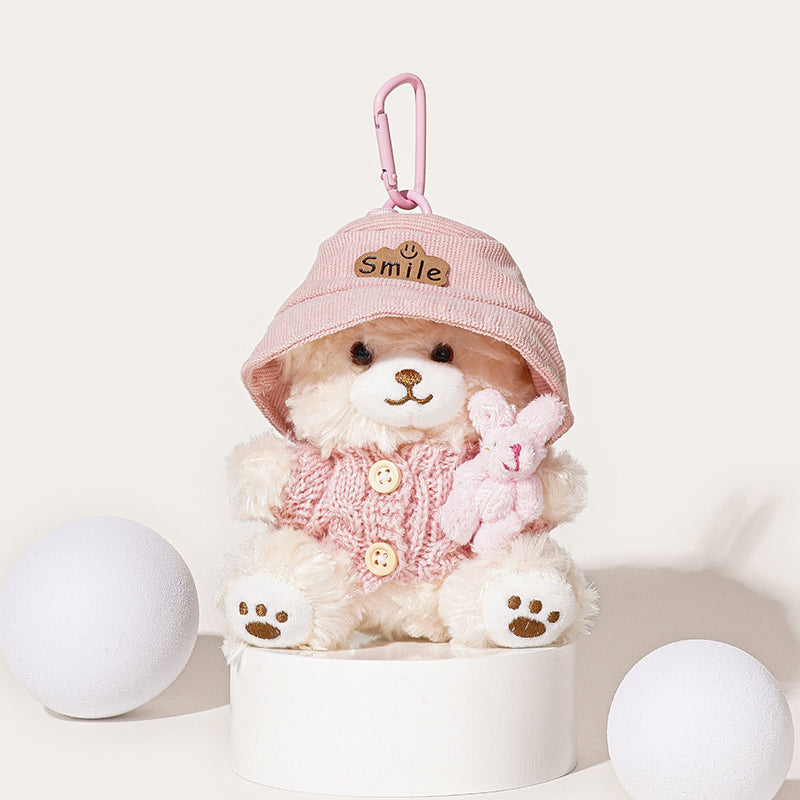 A white teddy bear plush keychain wearing a pink bucket hat with a "Smile" patch and a pink knit cardigan with buttons, holding a small pink rabbit plush, attached to a pink carabiner clip.