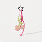 A pink leather cherry-shaped bag charm with a light green stem, attached to a pink braided rope strap. A black star-shaped clip is at the top, making it a trendy and cute accessory for bags or keychains.