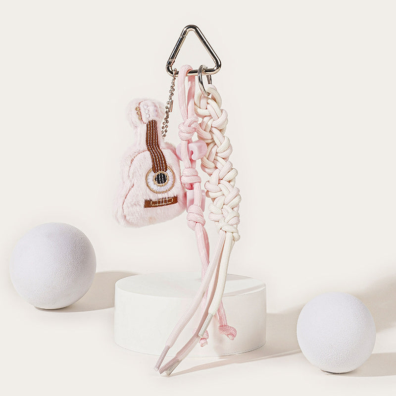 A pink plush guitar keychain with brown embroidered strings, attached to a silver carabiner with a pink and white braided rope strap and pink heart-shaped beads.