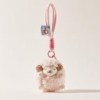 A fluffy pink sheep plush keychain with brown spiral horns and closed eyes hangs from a black tote bag strap, secured by a pink carabiner and a pink-wrapped cord.