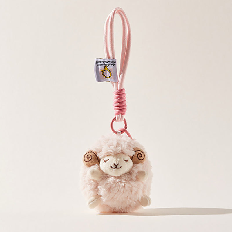 A fluffy pink sheep plush keychain with brown spiral horns and closed eyes hangs from a black tote bag strap, secured by a pink carabiner and a pink-wrapped cord.