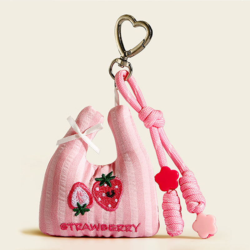 A pink striped fabric bag charm shaped like a mini tote, featuring embroidered strawberries and the word "STRAWBERRY", with a white bow and red flower beads on the strap.