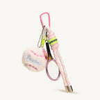 A pink tennis-themed keychain set, including a plush white tennis ball with pink stitching and a miniature pink racket, is shown against a plain white background, highlighting its design details.