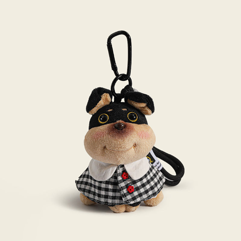 A plush dog bag charm dressed in a black and white plaid dress with red buttons and a white collar, attached to a black carabiner clip. The charm features a cheerful expression and is designed as a stylish and unique bag accessory.