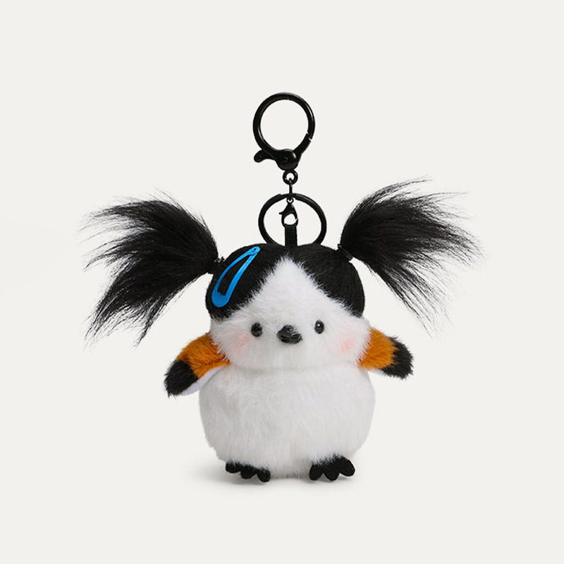 A plush bird keychain with a white body, black head, and orange-tipped wings. It has black, pigtails, a blue hair clip, and a black metal clasp.