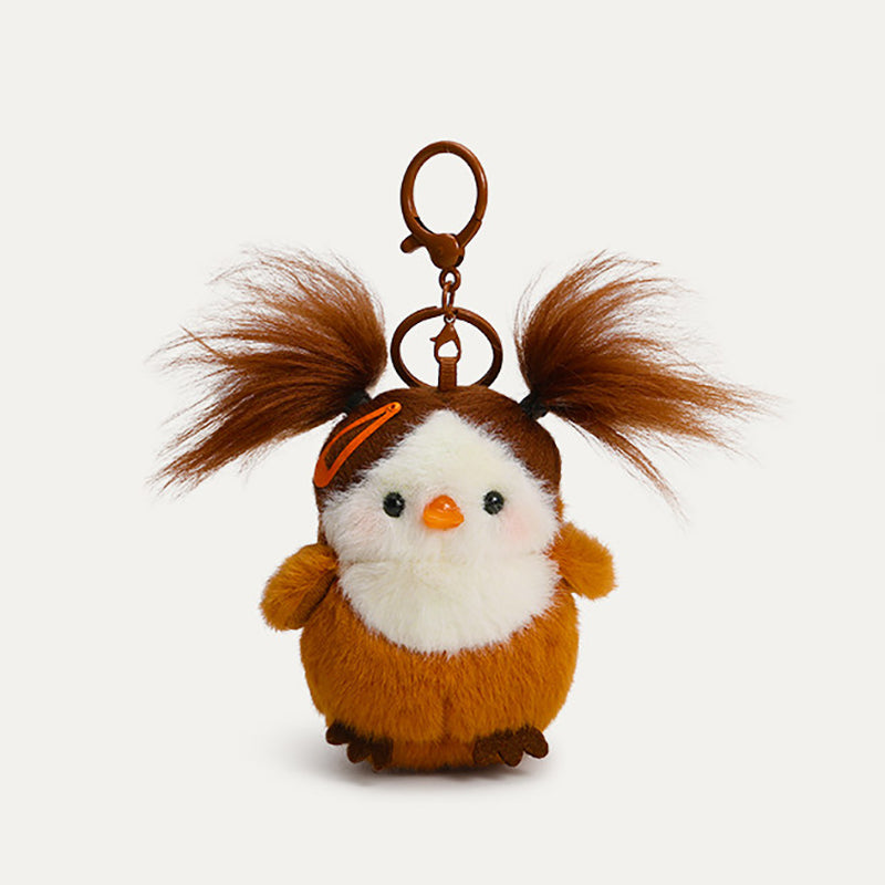 A plush bird keychain with an orange body, white chest, and brown head. It has brown, pigtails, an orange hair clip, and a brown metal clasp.