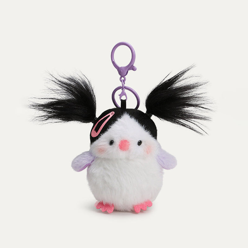 A plush bird keychain with a white body, black head, and lavender wings. It has black, pigtails, a pink hair clip, and a purple metal clasp.