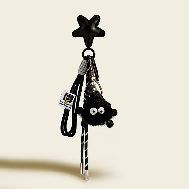 A black, fluffy monster charm with large googly eyes, hanging from a black leather star-shaped strap. It is attached with a black and white striped cord and features a small white tag with a logo.