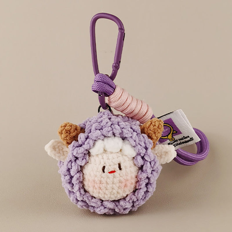 A purple crocheted sheep keychain with brown horns and a smiling face, attached to a purple carabiner clip and a brand tag.