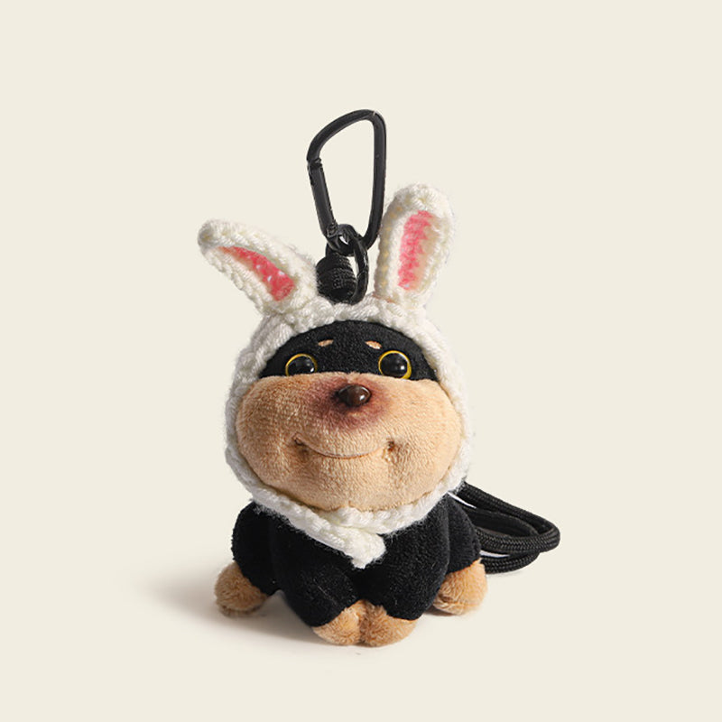 A plush dog bag charm with white crocheted rabbit ears featuring pink inner linings, attached to a black carabiner clip. This adorable accessory combines a playful animal theme with a soft, cuddly texture, perfect for personalizing bags or backpacks.