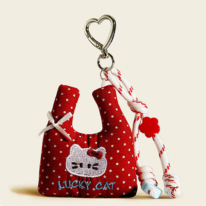 A front view of a red polka-dot fabric bag charm shaped like a mini tote, featuring an embroidered "LUCKY CAT" design and a white bow, with red-and-white rope and a red flower bead.