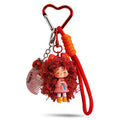 A red heart-shaped carabiner keychain featuring a cute doll with voluminous curly red hair, wearing a pink outfit. It includes a small comb charm inscribed with "Happy girl" and a braided red wrist strap.