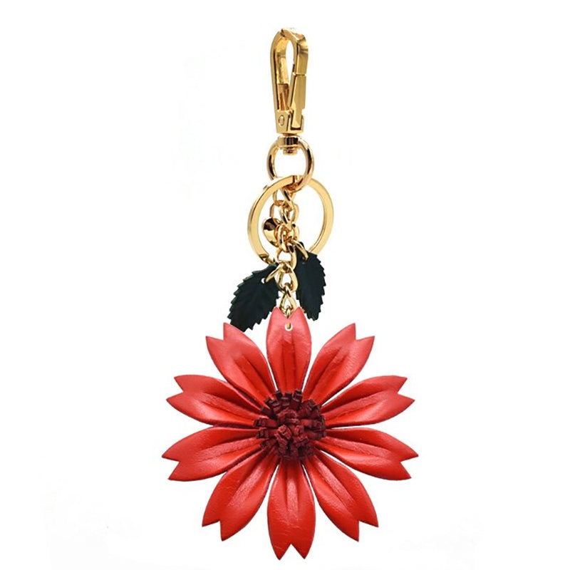 A vibrant red leather daisy pendant hanging vertically from a polished gold-tone carabiner. The flower’s center is detailed with stitched texture, and it is paired with dark green leaf charms.
