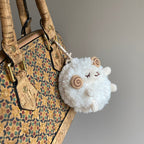 A side-angle shot of a white fluffy sheep plush keychain hanging from a cork-patterned bag, showing its round shape and soft texture.