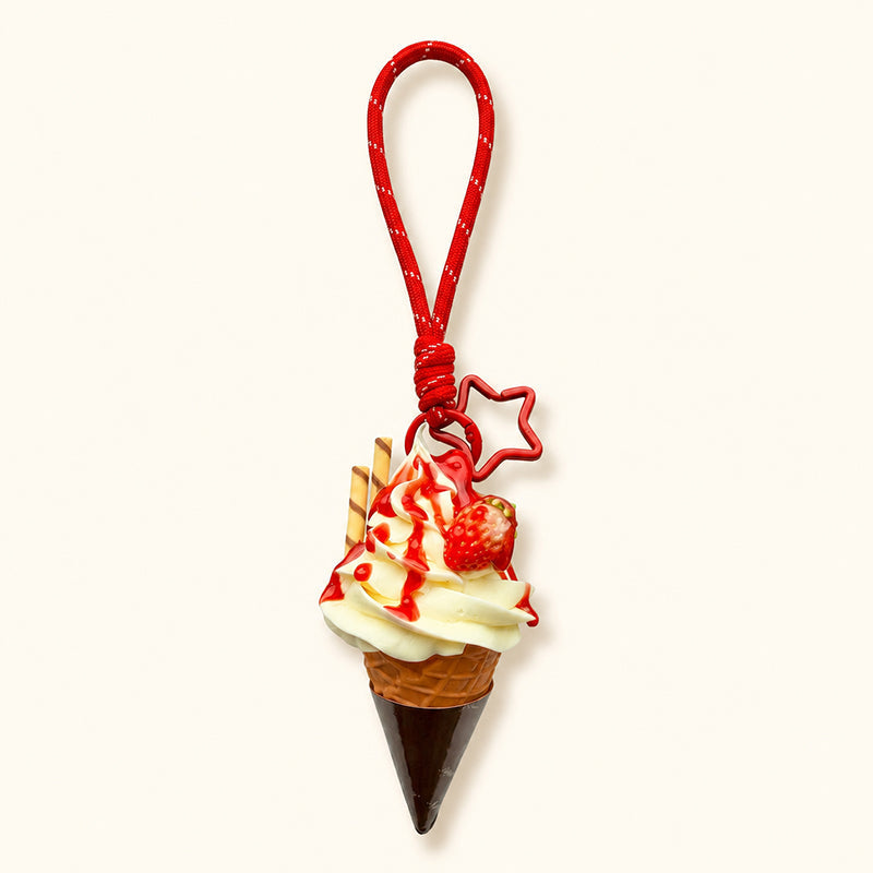 A detailed, realistic-looking ice cream cone charm with white cream swirls, red strawberry sauce, a small strawberry, and two waffle sticks. It is attached to a red braided rope with a star-shaped charm and a metal clasp, displayed against a plain white background.